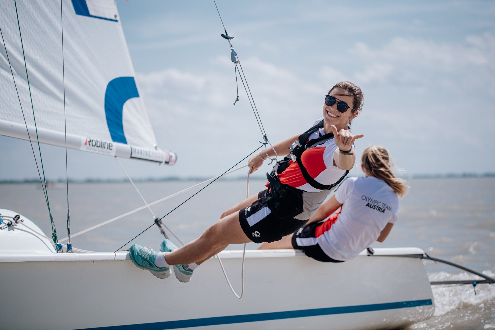 Cheerful sailor with sports sunglasses waves while hanging on the side of a sailboat