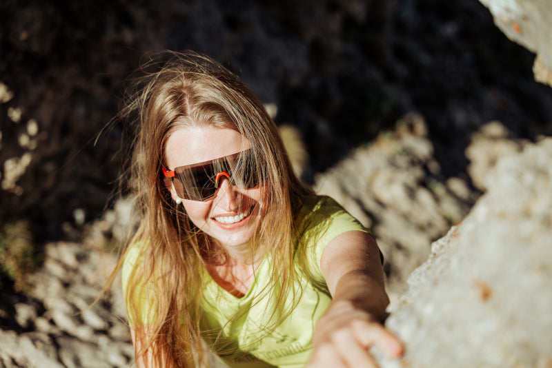 Smiling woman climbing up a rock on a sunny day, wearing sports sunglasses