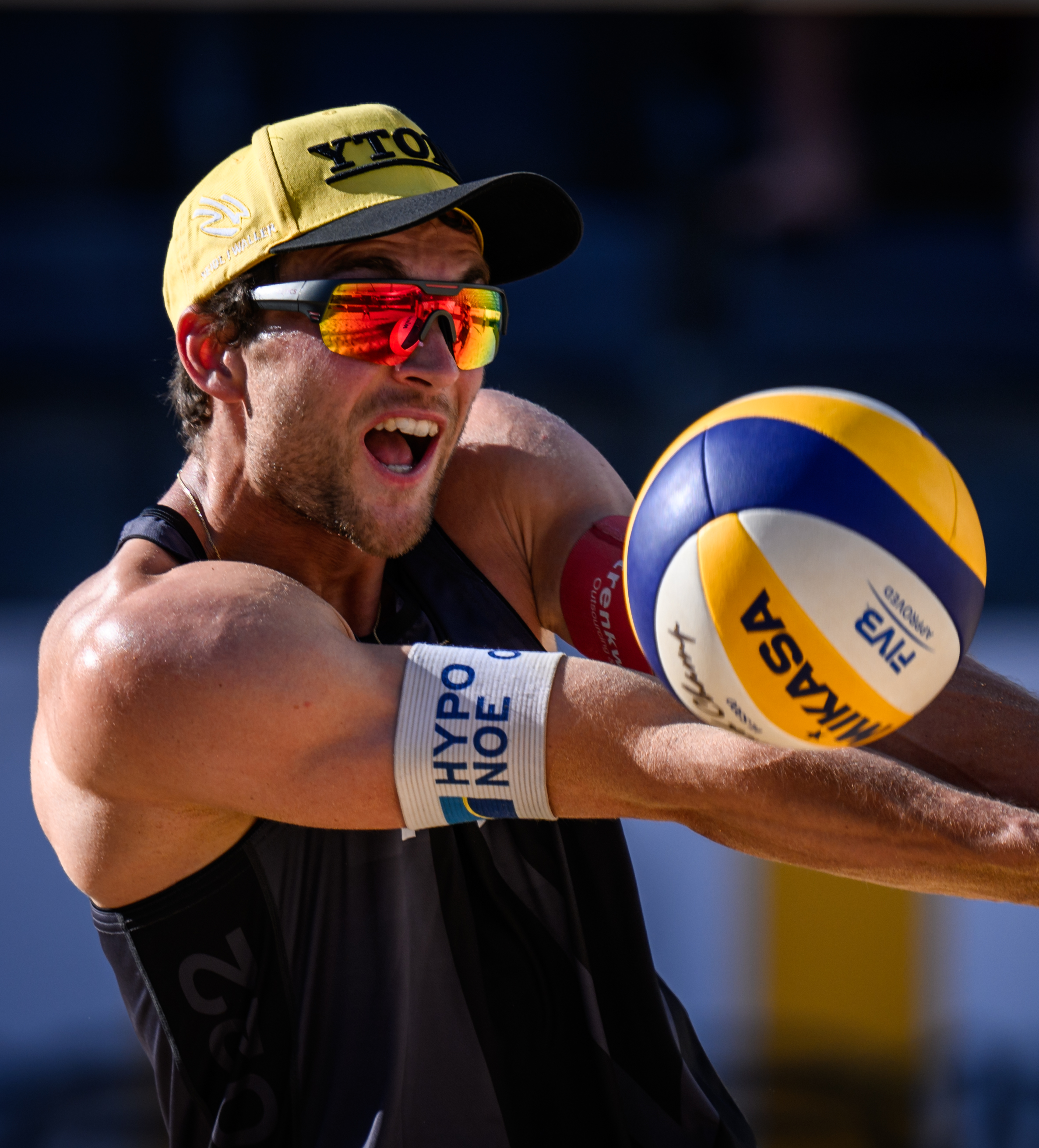 Male volleyball player with sunglasses and black tank top touching the ball