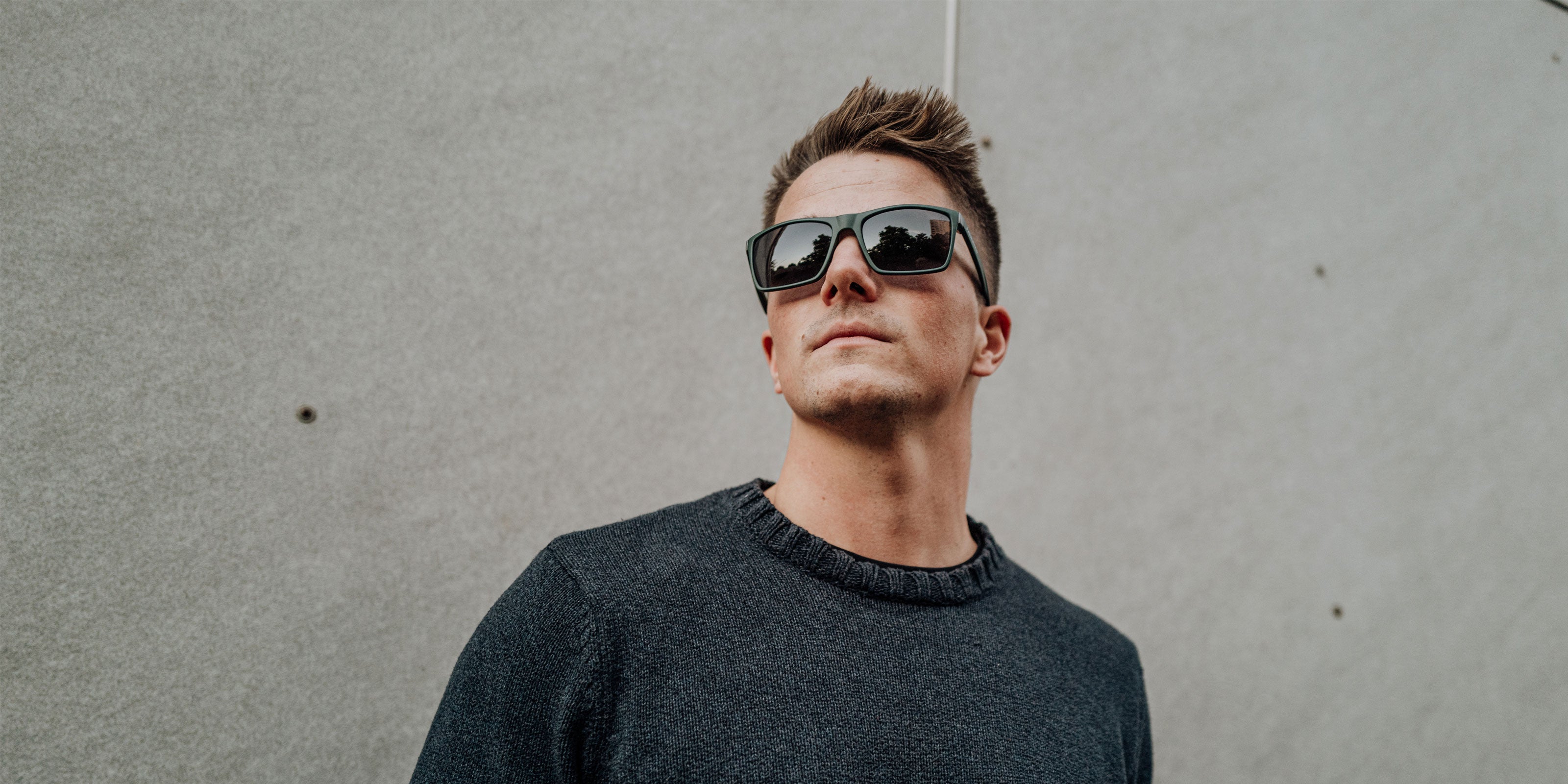 Modern man in dark sweater wears trendy sports-style sunglasses and looks thoughtful