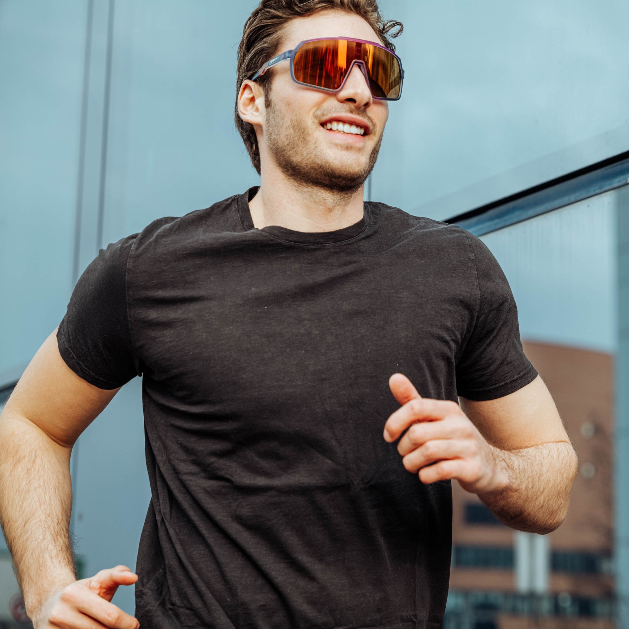Athletic man with modern running glasses runs smiling along a glass facade