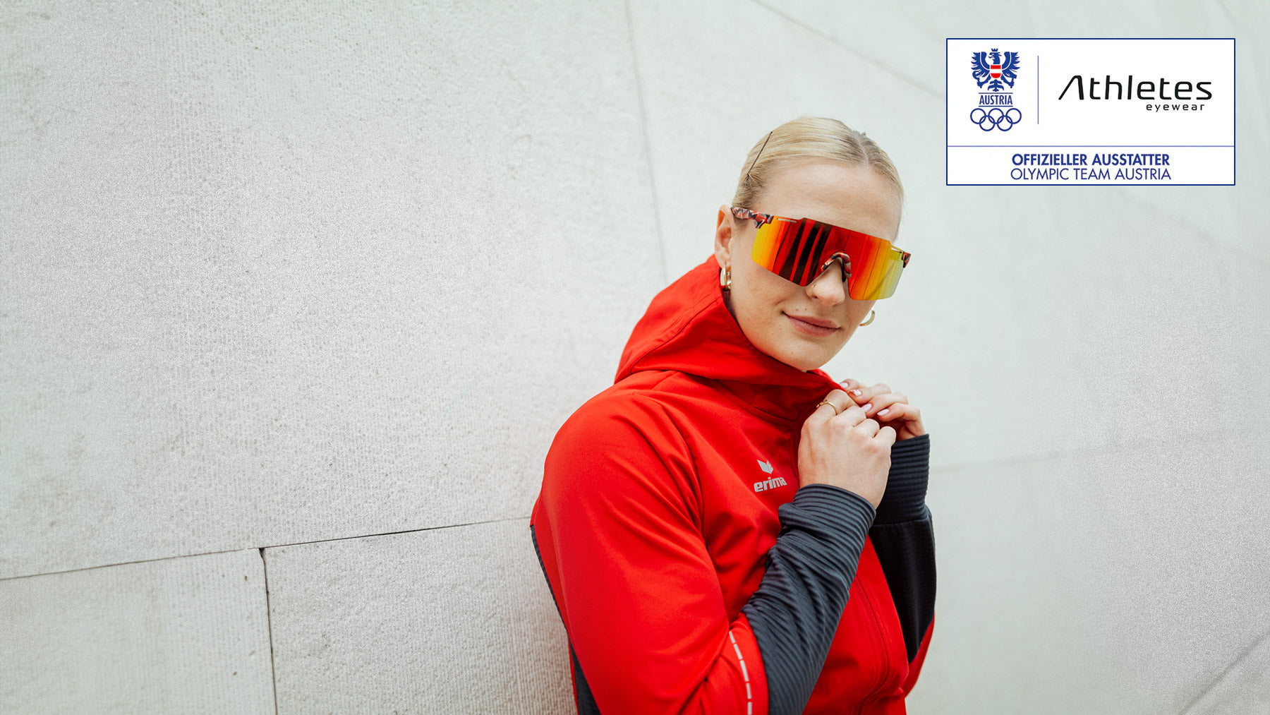 Frau des österreichischen Olympiateams trägt rote Sportjacke und sportliche Sonnenbrille