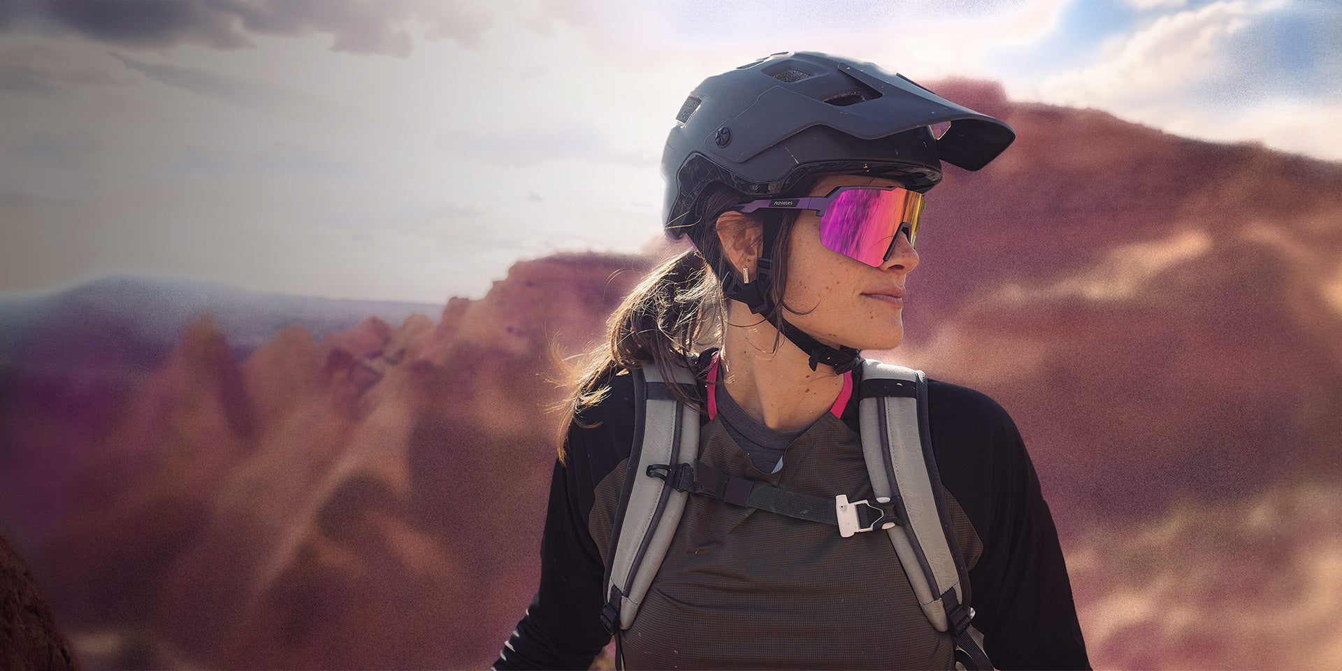 Bikerin mit stylischer Sportsonnenbrille und Helm vor bergiger Landschaft.